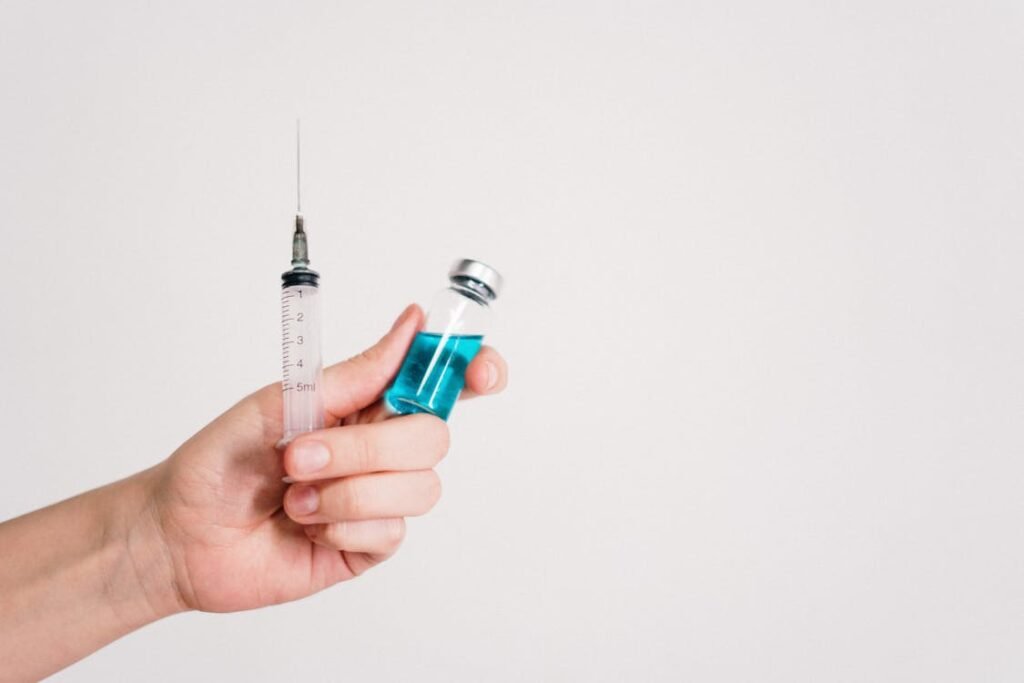 Free Hand holding a syringe and vaccine vial on a white background, symbolizing healthcare and immunization. Stock Photo